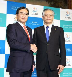 記者会見で握手する第四北越フィナンシャルグループの殖栗道郎社長（右）と群馬銀行の深井彰彦頭取＝２６日、東京都内のホテル