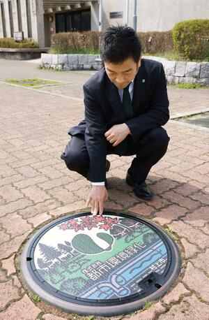村上市が設置した広告入りのマンホールふたと都市環境緑化の髙橋良夫社長＝村上市田端町