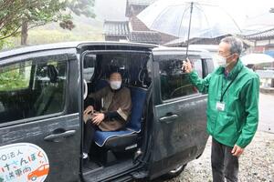 ボランティアによる有償旅客運送「さんぽくん」。雨が降る中、ボランティアの運転手が利用者に傘をさしかける=村上市中浜
