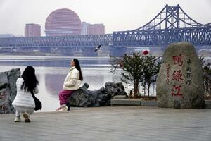 　中国遼寧省丹東で北朝鮮側を背景に記念撮影をする女性たち。中朝を結ぶ鉄道橋も見える＝１日（共同）