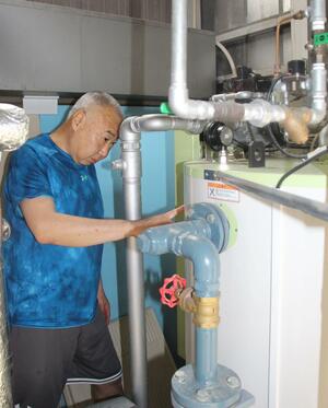  燃料高騰の影響を受ける県内の銭湯。ボイラー室で作業をする千鳥湯の熊谷孝さん＝新潟市中央区