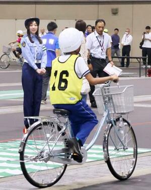 自転車の乗り方などを競う大会で、実技テスト中の参加者(手前)を見守る愛知県警交通安全大使の須田亜香里さん(奥左)=29日午前、名古屋市