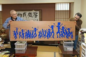 大阪・関西万博で6月に飾られる作品「PEOPLE」を手にする薄田東仙さん(左)=新潟市東区