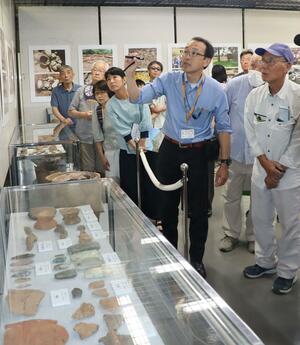 遺跡の出土品から推測される縄文時代の生活ぶりや島外との交流の説明に熱心に聞き入る参加者ら=佐渡市新穂瓜生屋