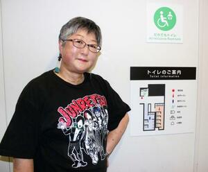 トイレの案内板の横に立つ百瀬まなみさん=5月、東京都渋谷区