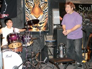 軽音楽に取り組む高校生を支援する本間純一さん(右)。自身もドラマーとして活動を続けている=佐渡市市野沢