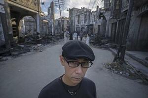 抗日戦争映画の巨大な撮影セットに立つ渋谷天馬。旧日本軍の攻撃で燃えた様子を再現した建物の横で、観光に来た多くの中国人親子が記念撮影していた=2025年8月、中国上海市(撮影・武隈周防、共同)