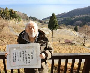 岩首の棚田を背に、緑白綬有功章の受章を喜ぶ大石惣一郎さん=佐渡市岩首