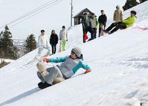 わら製のそり「ぼぼぞり」で滑るタイムを競った催し=20日、長岡市の古志高原スキー場