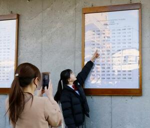 宮城県仙台一高の合格発表で掲示板の前で記念撮影をする受験生=3月、仙台市