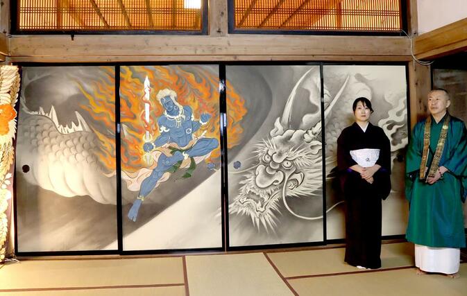 国上寺方丈講堂のふすまに描かれたイケメン絵巻第２弾。龍と不動明王の障壁画を背に立つ木村了子さんと住職の山田光哲さん＝１０日、燕市国上