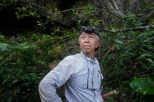 80年前の沖縄戦で激戦地となったガマの前に立つ具志堅隆松。当時の惨劇を思い浮かべながら遺骨収集活動を続ける=2025年7月、沖縄県糸満市(撮影・林昌三)
