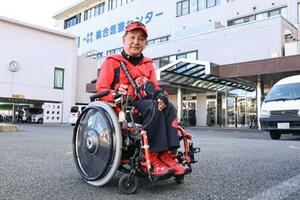 有園義肢の車いすを利用している胎児性水俣病患者の松永幸一郎さん。国保水俣市立総合医療センター(後方)でリハビリを続けている=2月、熊本県水俣市