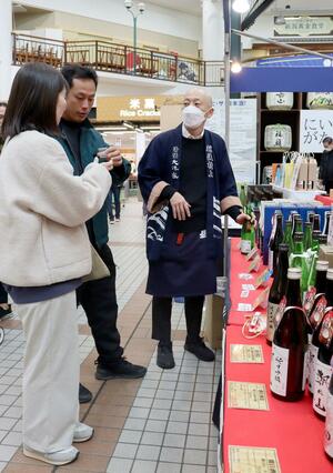 年末年始市で県内酒蔵の日本酒を試飲する買い物客＝29日、新潟市西区山田