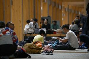 8月、大阪メトロ中央線が運転見合わせとなり、未明に万博会場の大屋根リングの下で休む来場者ら=大阪市此花区の夢洲