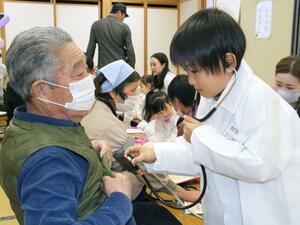 住民男性の胸に聴診器を当て、心音検査をするキッズドクター=村上市高根