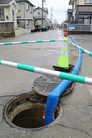 地震で被害が出た下水管の応急措置として道路上に渡された仮設ホース=18日、新潟市西区鳥原