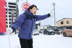 雪景色の中、道行く歩行者やドライバーに笑顔であいさつした内山航さん＝９日、新潟市中央区米山