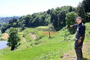 棚田を指し示す阿久澤剛樹さん。中央に水のない田んぼが見える=5月18日、十日町市松代蒲生