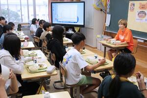 金沢みどり選手(右)と一緒に給食を食べる水原小児童=阿賀野市岡山町