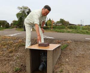 ふたが盗まれた給水栓の上に、合板で手作りした板をかぶせる髙野幸夫さん=上越市吉川区