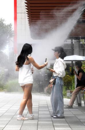 梅雨明けした東京・銀座でミストを浴びる人たち=18日午前