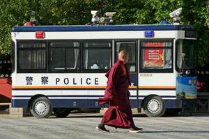 チベット仏教寺院の敷地内に止められた警察車両の前を歩く僧侶=2日、中国青海省西寧市(共同)