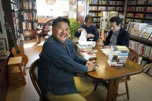 「あおぞら古書店」で利用者と書籍の値札付けなどをする金田恵郎(手前)。テーブルは近隣住民の憩いの場にもなっている=2025年10月、兵庫県宝塚市