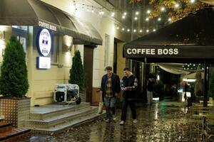 ウクライナ北部チェルニヒウで、停電中に発電機を使って営業するカフェの前を歩く若者=10月(ロイター=共同)