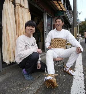 　御燈祭りの日、堅田裕見子（左）の家を訪れ、荒縄を巻いてわらじを履いた北原潤希。わらじ作りの作業場の家屋（後方）には、たいまつがつり下げられていた＝２０２６年２月、和歌山県新宮市