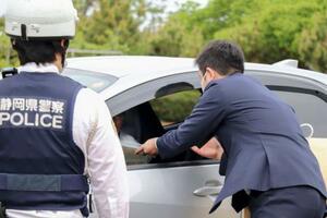 　通行車両を呼び止め、情報提供を求めるチラシを配布する静岡県警の捜査員＝２１日午前、浜松市中央区