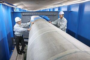 有明大橋の下にある内径1メートル超の水道管の塗装を確認する新潟市水道局の五十嵐司さん(右)=新潟市