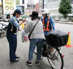 自転車利用者に啓発用のチラシを配る警察官=4日午前、東京都新宿区