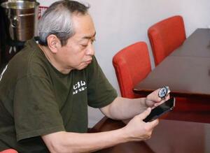 「コミサポひろしま」のメンバーに見つけてもらった遺品の腕時計とスマートフォンを見つめる楠健二さん=10日、川崎市の居酒屋「わじまんま」
