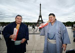 大相撲パリ公演を前に、エッフェル塔の前でフランスパンを食べる大の里(右)と豊昇龍の両横綱=11日、パリ(共同)