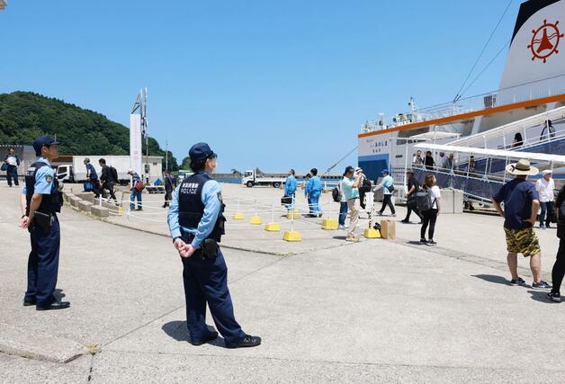 粟島汽船のフェリーから下船する来島者を見守る臨時交番の警察官=11日