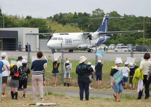 着陸したトキエアの機体を出迎え、手を振る地元・両津吉井小児童ら＝２８日、佐渡空港
