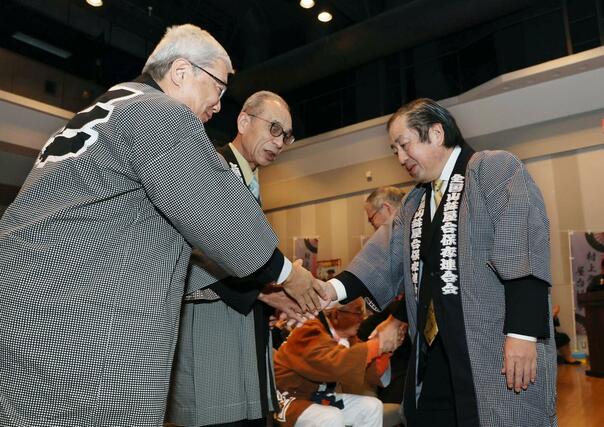 追加登録が決まり、握手を交わす村上まつり保存会会長の渡邉明さん(右)ら=11日、村上市
