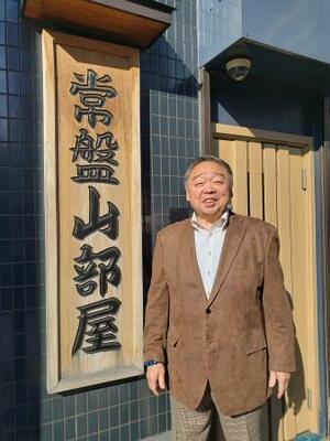 ２０２５年１２月、部屋の看板前に立つ常盤山親方＝東京都板橋区の常盤山部屋