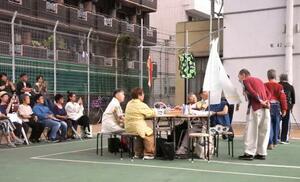 シニア女性が手仕事をしている所に、ファッションショーの男性モデルが立ち寄って言葉を交わす=大阪市西成区